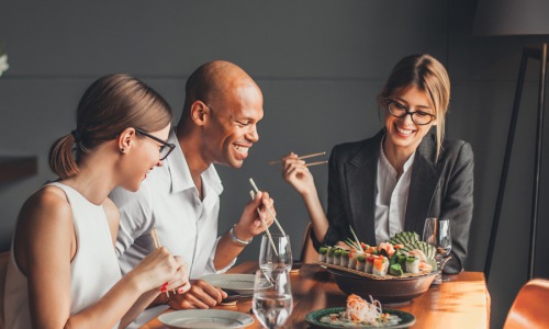Three people enjoying sushi and conversation at a modern restaurant dining table.